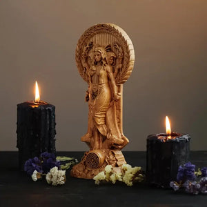 Wooden figurine of a woman with a wreath, flanked by two lit black candles on a dark surface. auraworks decor