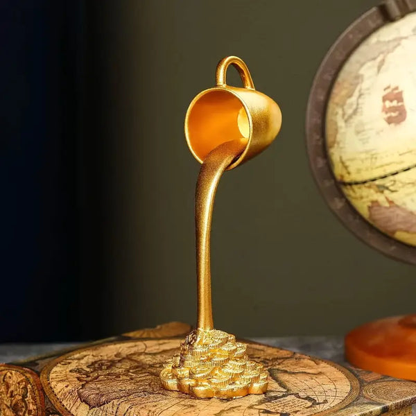 Gold sculpture of a cup pouring liquid onto a world map  decor aura works