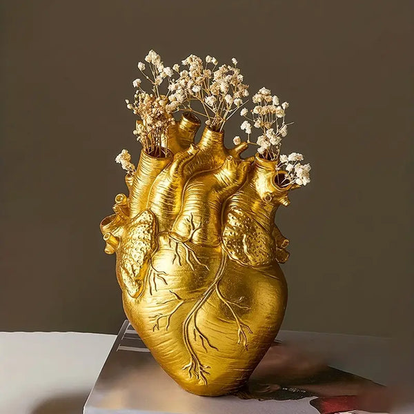 Gold heart-shaped vase with floral arrangement on a white surface against a dark background