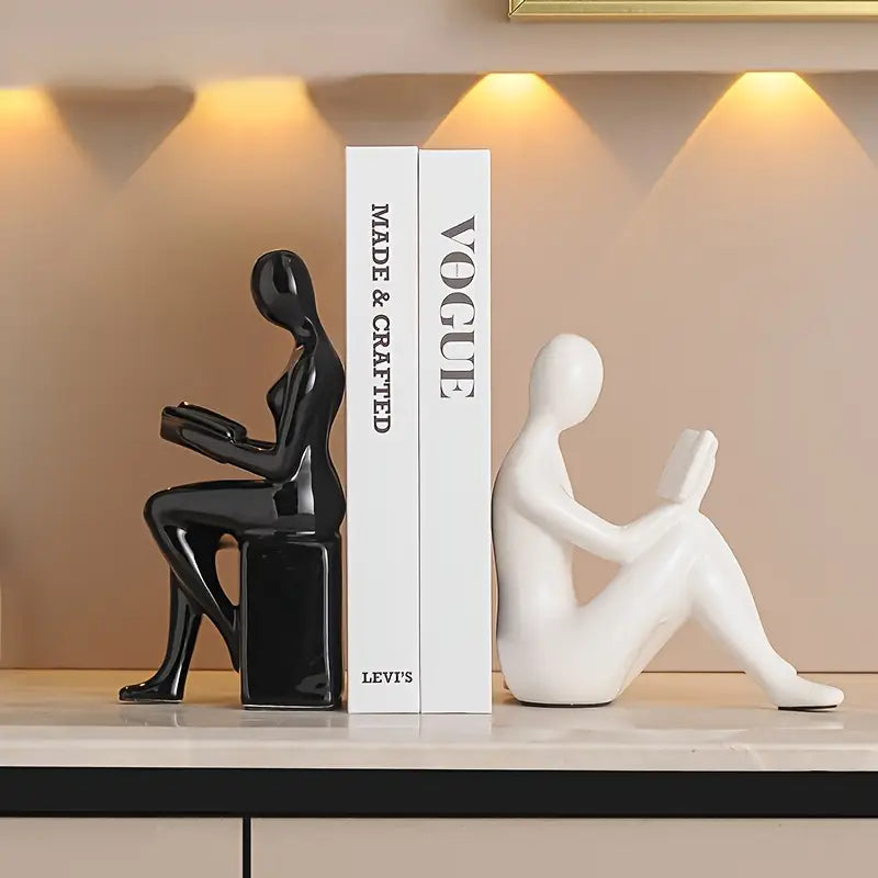 Gold human-shaped bookends on a reflective surface with books in the background. auraworks decor