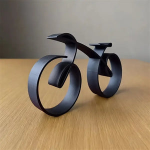 Black metal bicycle sculpture on a wooden surface with a gray background decor aura works