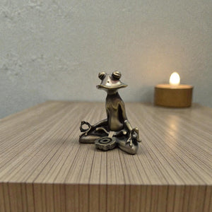 Bronze frog sculpture in a meditative pose on a wooden surface with a candle in the background.