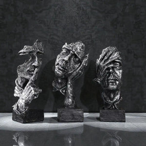 Three bronze sculptures of stylized faces on a reflective surface with a dark textured background Aura Works Decor