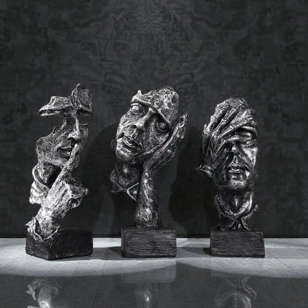 Three bronze sculptures of stylized faces on a reflective surface with a dark textured background Aura Works Decor