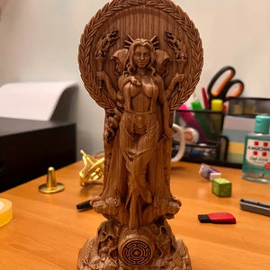 Wooden statue of a deity between two lit candles on a dark surface with  flowers. auraworks Decor