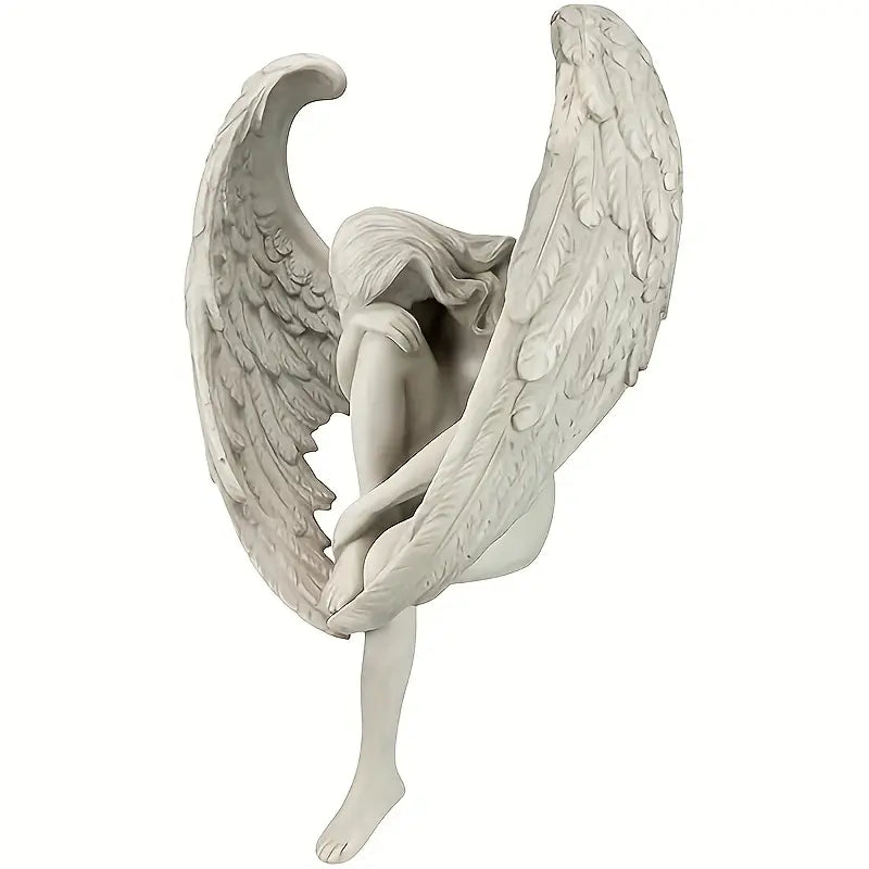 Winged Grace Angel statue in white resin, sitting with folded wings on a wooden table next to a pink rose bouquet – elegant spiritual home decor. Auraworks