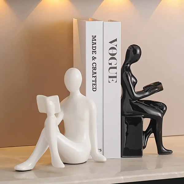 Two ceramic figures, one white and one black, sitting on a shelf with a 'Vogue' book in the background. decor aura works