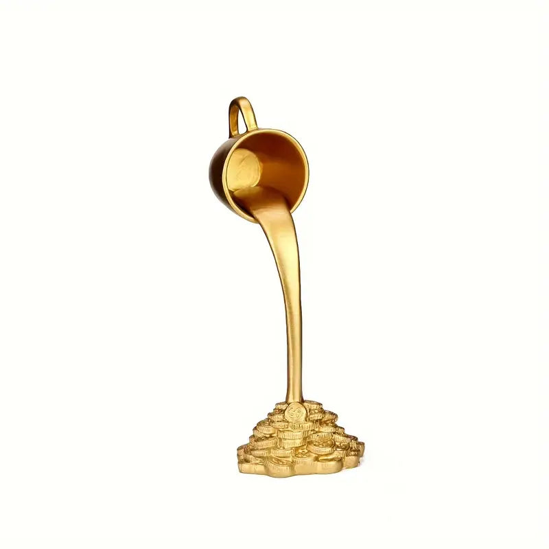 Gold decorative item resembling a teacup pouring gold coins on a textured surface with a book in the background. auraworks decor