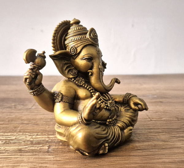 Left view of a handcrafted brass Lord Ganesha idol in a blessing pose, seated peacefully with intricate detailing, placed on a white cloth background — perfect for home decor, spirituality, and gifting. auraworks
