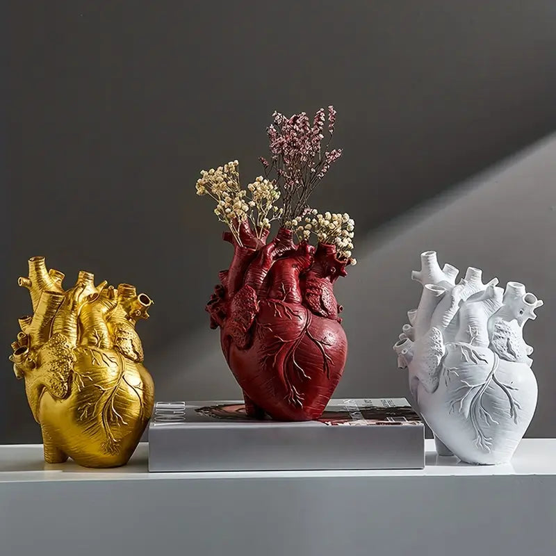 Three heart-shaped vases in gold, red, and white on a gray surface with a dark background. auraworks deccor