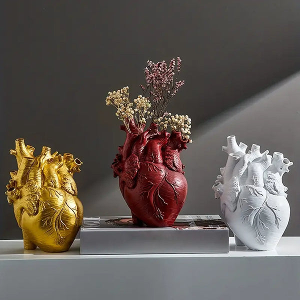 Three heart-shaped vases in gold, red, and white on a gray surface with a dark background. auraworks deccor
