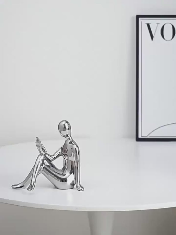 Gold human-shaped bookends on a reflective surface with books in the background. auraworks decor